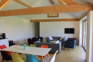 Groepsruimte vóór: witte eettafel met gekleurde kuipstoelen en losse zitjes onder de dakbalken