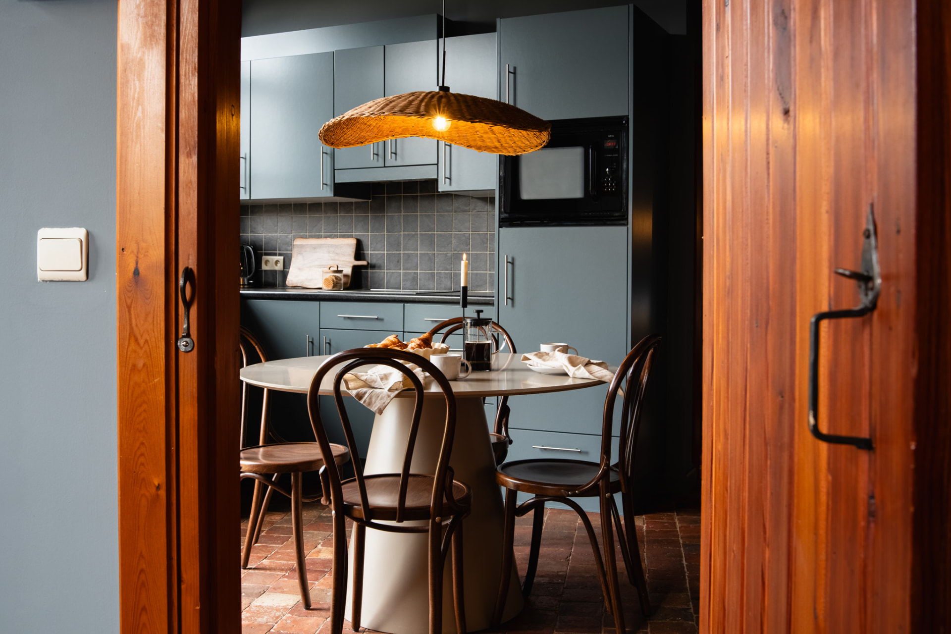 Keuken na: grijsblauw geschilderde keuken met rieten hanglamp, ronde tafel en Weense stoelen