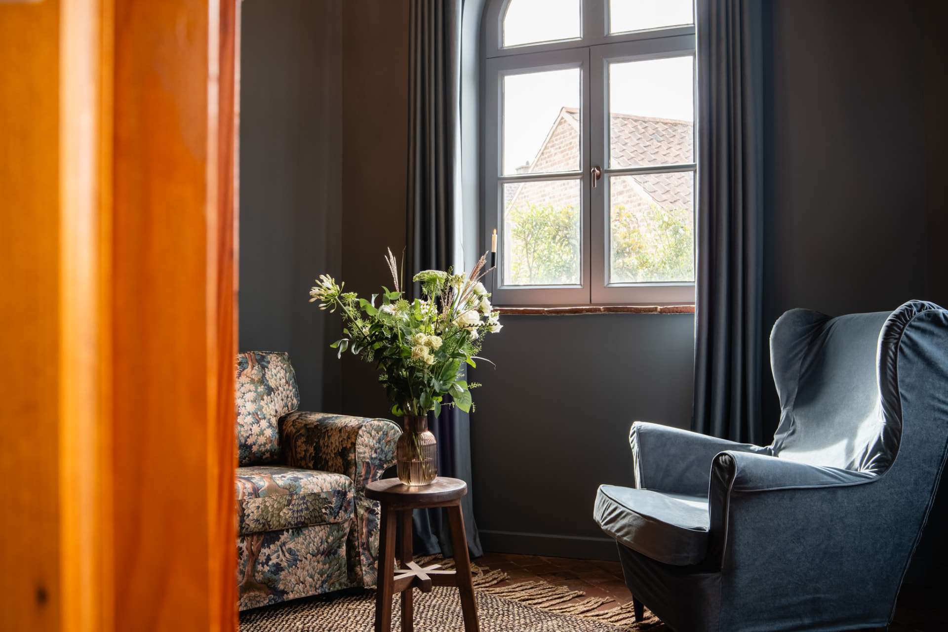 Zithoek bij het boogvenster met bloemenfauteuil, blauwe oorfauteuil en een groot boeket