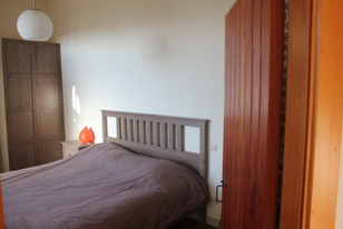 Slaapkamer vóór: eenvoudig houten bed met bruin dekbed tussen kastwanden
