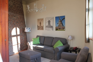 Woonkamer van Molen de Hoop vóór de herinrichting, met grijze bank, groene kussens en ingelijste molenprints