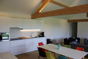 Keuken vóór: witte greeploze keukenwand met eettafel en gekleurde stoelen